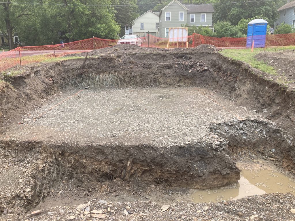 Looking over a dug out foundation with a house in the background.