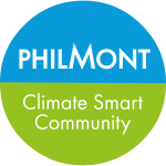 A circle with a robin's-egg-blue hemisphere over a grass-green hemisphere and white print saying "Philmont Climate Smart Community" with the "M" of "Philmont" creating mountain peaks.