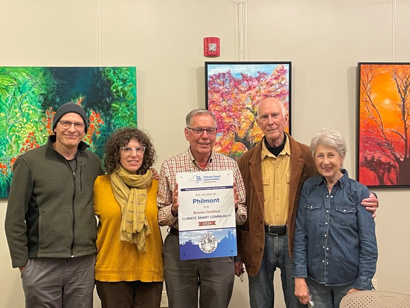 Five people standing together standing in front of vibrantly colored paintings holding a a sign